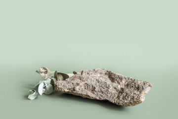Natural gray stone stand for presentation and exhibitions on pastel green background. Abstract podium for organic cosmetic products with green leaves. Minimal style.