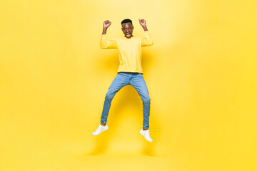 Fototapeta na wymiar Surprised excited African man jumping with hands raised in studio yellow color isolated background