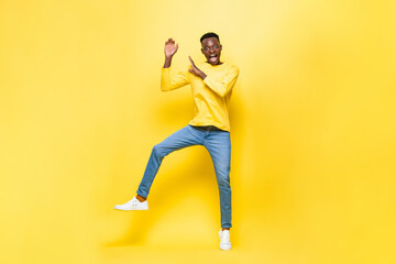 Fototapeta na wymiar Shocked African man jumping with hands raised in studio yellow color isolated background