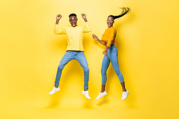 Fototapeta na wymiar Surprised excited African couple jumping in studio isolated yellow color background