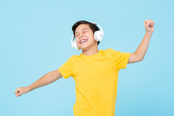 Happy mixed race boy listening to music on headphones and dancing in studio light blue isolated...