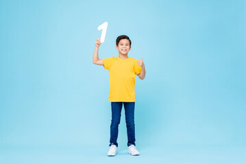 Cute mixed race boy giving thumbs up and holding number one in isolated light blue studio background