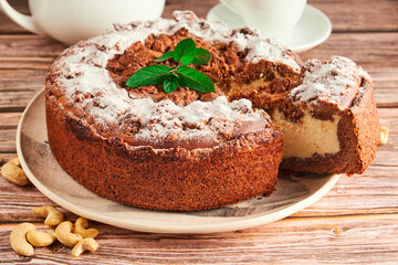 Homemade round cake on a plate, so fresh and delicious with ingredients: eggs, flour, cocoa on a wooden table. Home baking concept for background and wallpaper.