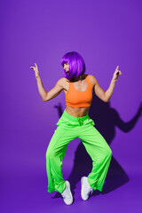 Carefree woman dancer wearing colorful sportswear having fun against purple background