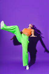 Active woman dancer wearing colorful sportswear performing against purple background