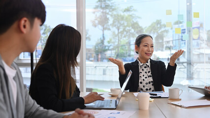 Concentrated middle aged female team leader explaining project details to young employees at meeting
