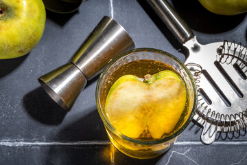 Apple cider cocktail. Raw apple vinegar cocktail garnished with apple slice, with bar utensils,...