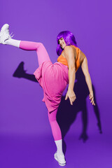Carefree woman dancer wearing colorful sportswear performing against purple background