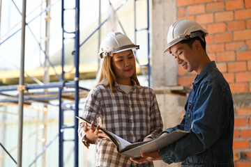 Two architects wearing safety helmet working on blueprints at construction site