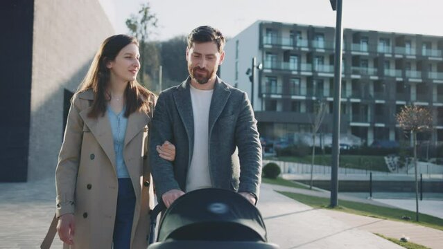 Close up young family walking with a pram. Husband and wife with new born baby. Smiling at sunlight. Parenthood. Slow motion