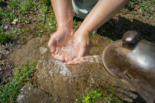 Close-up of women's hands folded by a boat under pouring cold drinking water from a water column. A woman collects water from a drinking column. Selective focus