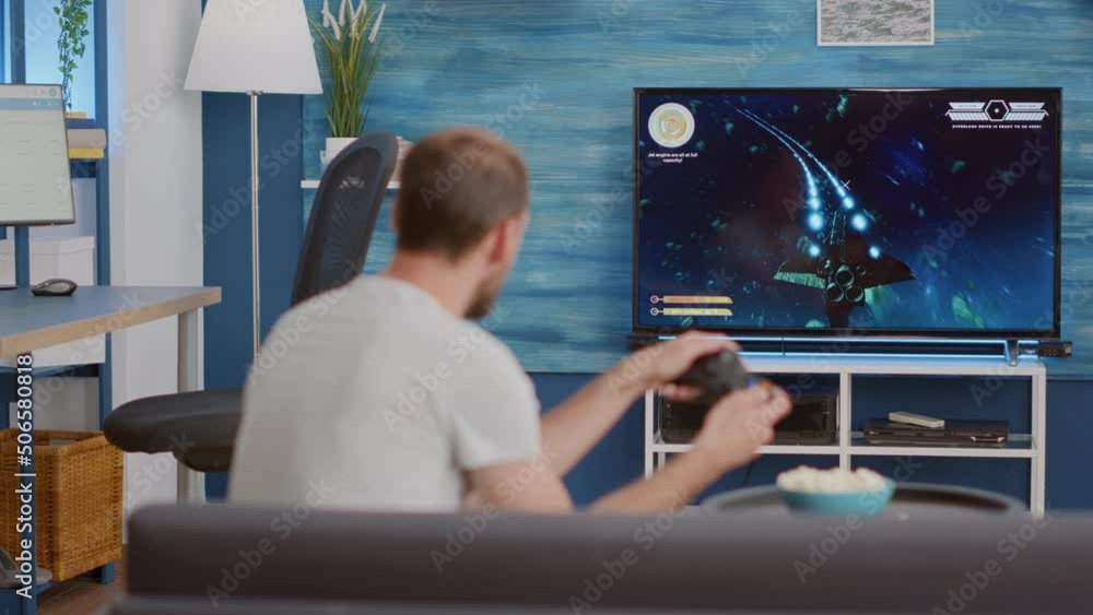 Poster man holding wireless controller playing console video game first person shooter on tv while sitting 