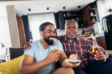 Excited old father and son watching tv,drink beer, having fun at home