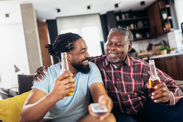 Excited old father and son watching tv,drink beer, having fun at home