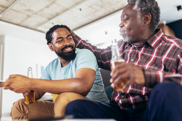 Excited old father and son watching tv,drink beer, having fun at home