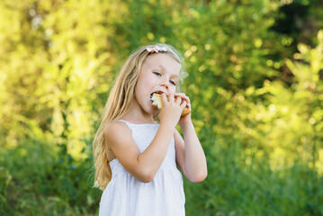 Little girl eats a bun in the summer park close-up portrait. Fast food on the street. snack
