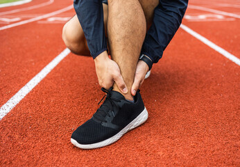 Fototapeta premium Young man runner has sore ankles because he ran too long. Male Exercising until the injury. Overtrained. Young sport man accident running on track