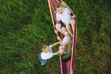 Two boys and a girl preschoolers play and ride in a bright striped hammock in a park in nature on a...