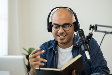 Content creator asia man host streaming his a podcast on laptop with headphones and condenser microphone interview guest conversation at home broadcast studio. Male blogger recording voice over radio