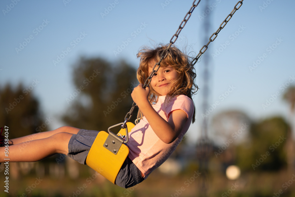 Wall mural little boy having fun on a swing on the playground in public park on summer day. happy child enjoy s