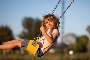 Little boy having fun on a swing on the playground in public park on summer day. Happy child enjoy...