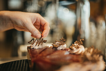 Hand placing down a chocolate decoration on top of chocolate cake with whipped cream