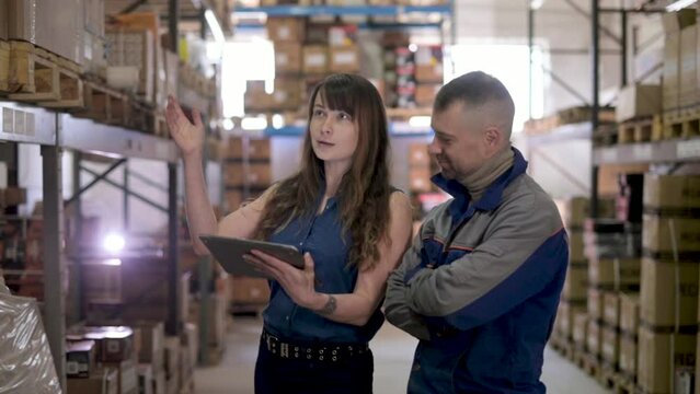 Workers inside warehouse check delivered cargo with waybill. female manager in a large warehouse distribution retail center explains to employee arrangement of cardboard boxes on shelves