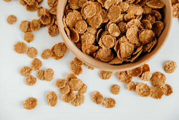 Crispy healthy dry cereal flakes in a wooden bowl on white background