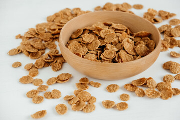 Crispy healthy dry cereal flakes in a wooden bowl on white background