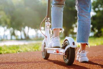 Woman riding electric kick scooter outdoors at sunset, closeup. Ecological transportation concept. © maxbelchenko