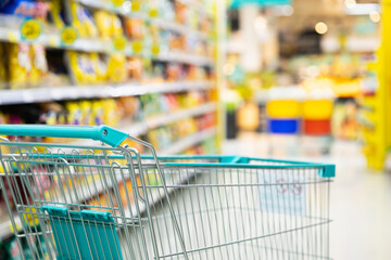 Supermarket aisle with empty green shopping cart. Trolley cart at the product shelf in the...