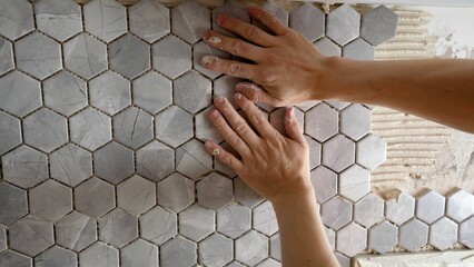 The master glues a mosaic of ceramic tiles. The worker presses the tile with his hands while gluing...