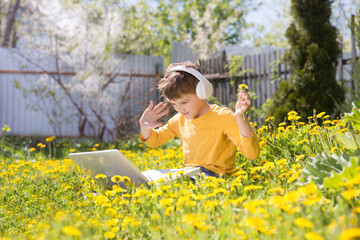 homeschooling, distant learning. Chatting with Friends, Studying School Homework. preteen boy in headphones using a laptop, connecting to the Internet outdoors at yard.