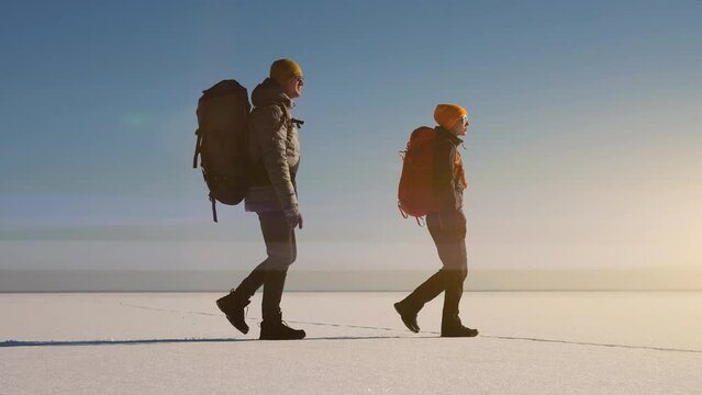 The two explorers with backpacks going through the snow field. slow motion
