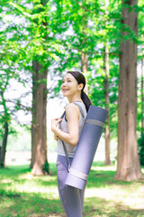 森の中でヨガマットを持つ女性　森林ヨガ　パークヨガ