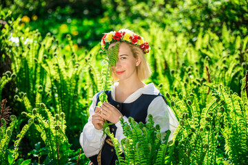 Young woman in national clothes and wreath against the background of a green fern. Ligo Latvian holiday