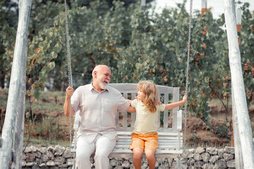 Grandfather and son swinging in garden. Granddad and grandchild playing on swing. Generations ages.