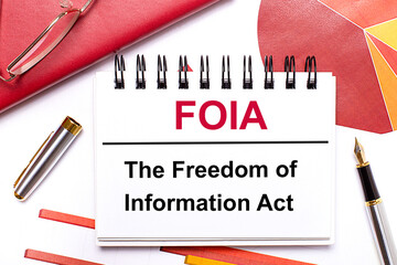 On the desktop is a white notebook with the text FOIA The Freedom of Information Act, a pen,...