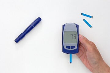 Top view of cropped woman hand holding glucometer with 7.3 result on display with blooded test strip inside, lancet and test strips on white background