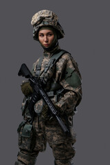 Studio shot of isolated on gray background woman soldier holding rifle.