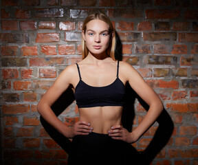 Young beautiful woman dressed in sportswear posing against a red brick wall.