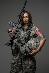 Photo of brown haired female soldier dressed in camouflage uniform holding rifle on her shoulder.