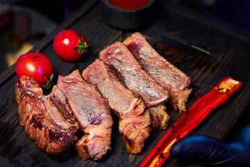 The waiter holds a dish with steak with sauce, tomatoes and red hot peppers