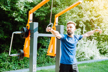 Chest workout with band crossovers. Charismatic man doing exercise on the outdoor exercise machine. Working out the pectoral muscles.