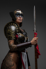 Studio shot of seductive woman barbarian dressed in armor and helmet holding spear.
