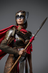 Shot of female ancient fighter with red cloak and brown hairs holding spear.