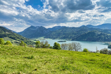 Overlooking lake Schliersee in the Bavarian Alps in southern Germany with lush green grass in the foreground and dramatic clouds over the mountains in the background on a perfect spring or summer day