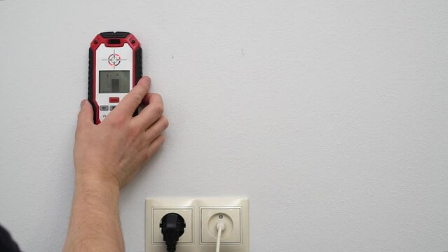 Man using stud finder to locate framing studs located behind the walling surface. Using a wall scanner to identify hidden electrical wiring. Space for text.