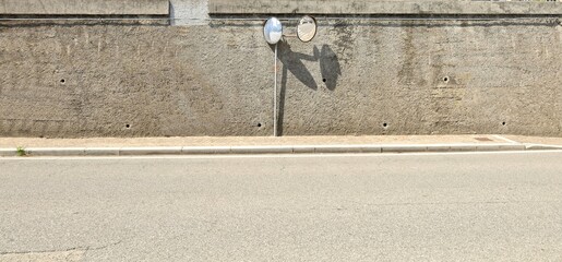 Rough concrete wall with two traffic wide angle security convex mirrors on a pole. Sidewalk and asphalt road in front. Background for copy space