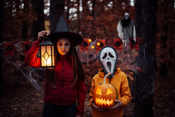 Children in halloween costumes with pumpkin in dark spooky forest. Small boy in mask of a ghost,...